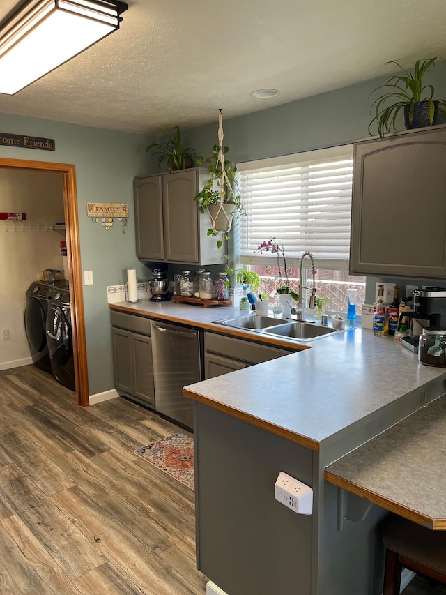 kitchen featuring a sink, separate washer and dryer, a peninsula, wood finished floors, and stainless steel dishwasher