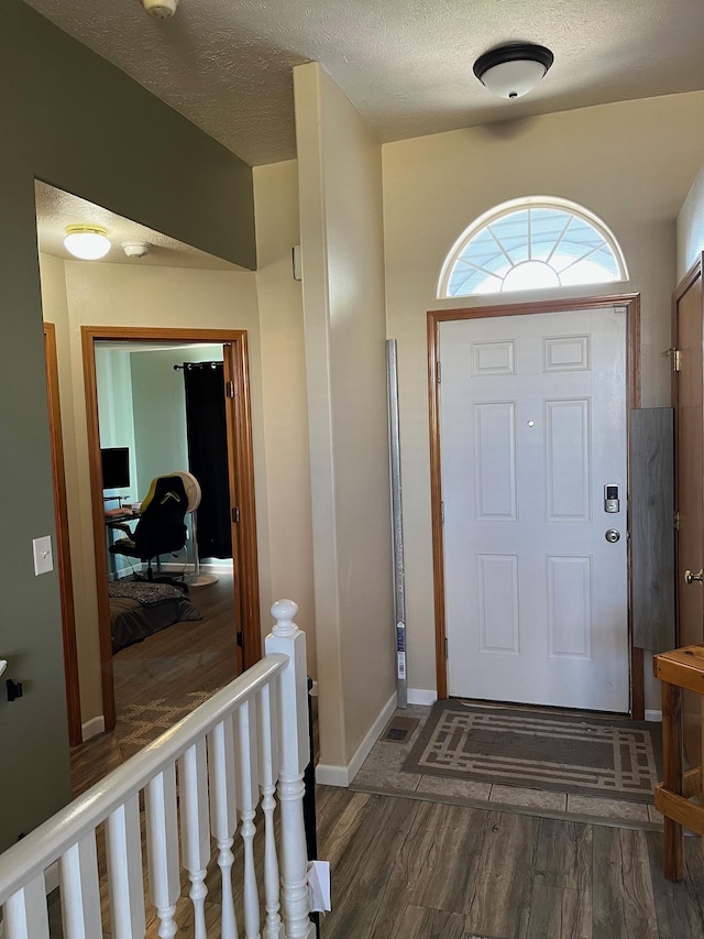 foyer entrance with a textured ceiling, baseboards, and wood finished floors