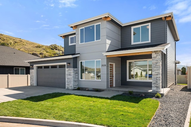 modern home with stone siding, a front lawn, concrete driveway, and fence
