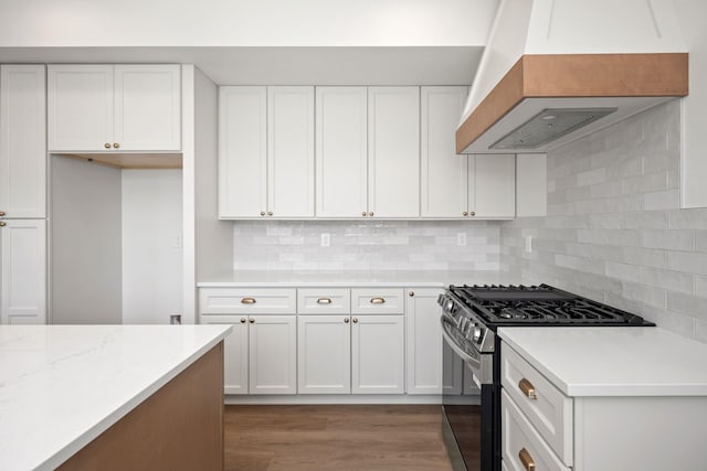kitchen featuring custom exhaust hood, wood finished floors, decorative backsplash, white cabinets, and stainless steel range with gas stovetop