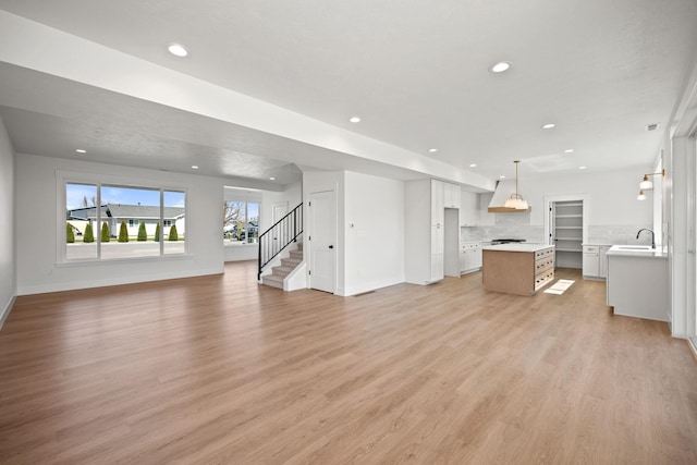 unfurnished living room with recessed lighting, light wood-style flooring, baseboards, and a sink