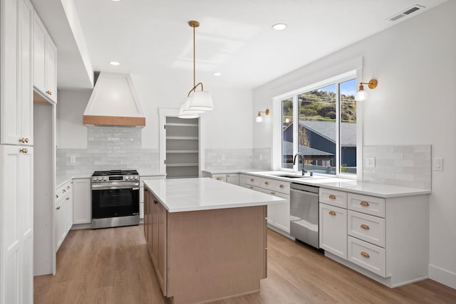 kitchen featuring stainless steel appliances, a sink, light wood-type flooring, visible vents, and custom range hood
