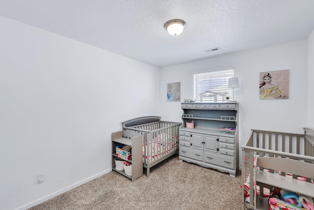 carpeted bedroom featuring a nursery area, baseboards, a textured ceiling, and visible vents