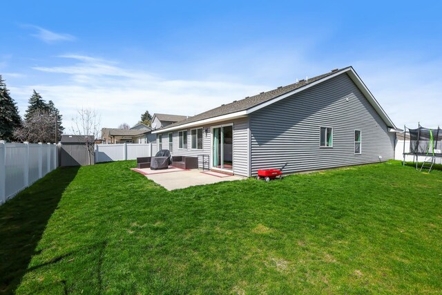 rear view of property featuring a lawn, a patio area, a fenced backyard, and a trampoline