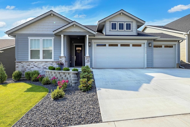 craftsman-style home featuring concrete driveway, stone siding, a shingled roof, an attached garage, and a front yard