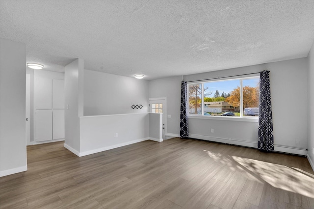 unfurnished room with a baseboard heating unit, baseboards, wood finished floors, and a textured ceiling