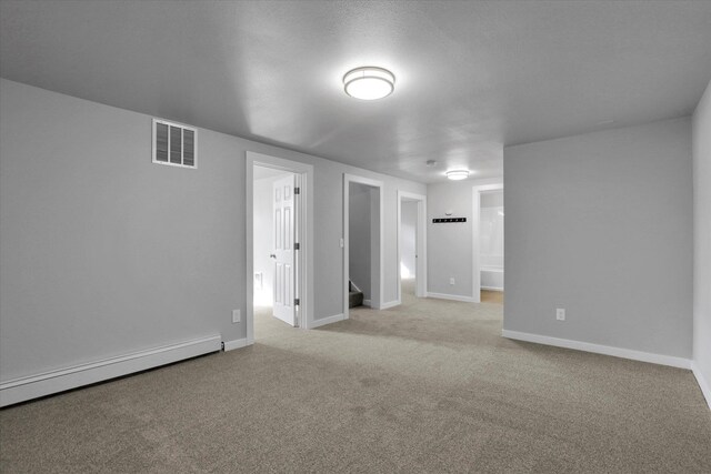 unfurnished room featuring a baseboard heating unit, light carpet, visible vents, and baseboards