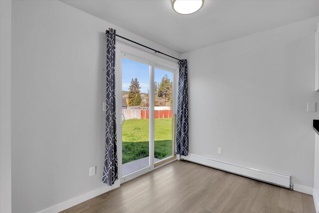 unfurnished dining area with baseboards, wood finished floors, and a baseboard radiator