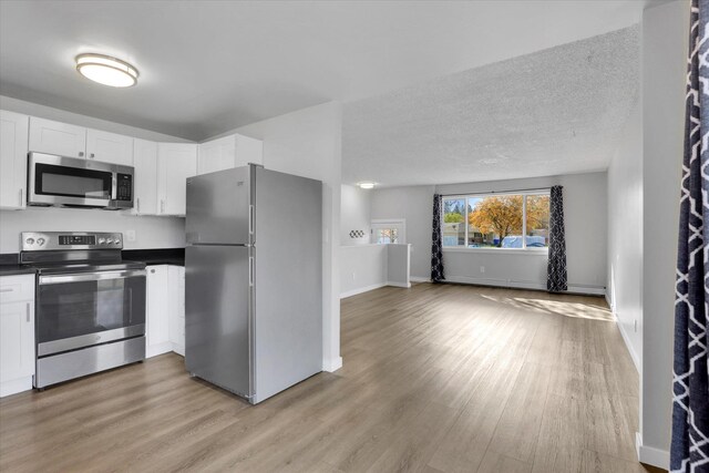 kitchen with dark countertops, light wood-style flooring, appliances with stainless steel finishes, open floor plan, and white cabinetry