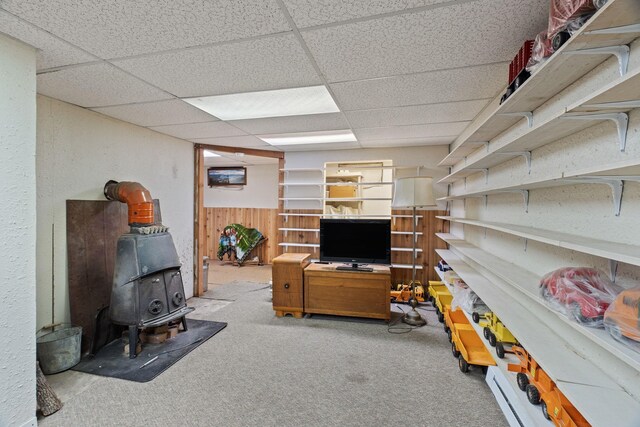 interior space featuring wooden walls, a wood stove, carpet flooring, and a drop ceiling
