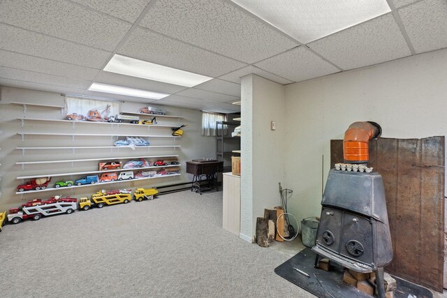 interior space with carpet floors, a wood stove, and a drop ceiling