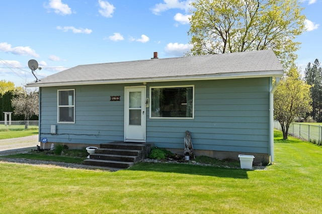 bungalow-style house featuring a shingled roof, a front lawn, and fence