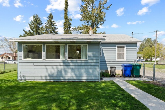 back of house featuring a lawn, fence, and roof with shingles