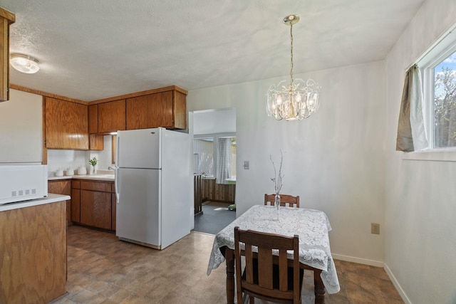 kitchen with light countertops, white appliances, baseboards, a chandelier, and brown cabinetry
