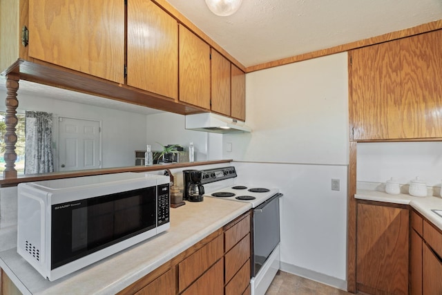 kitchen with brown cabinets, under cabinet range hood, white appliances, and light countertops