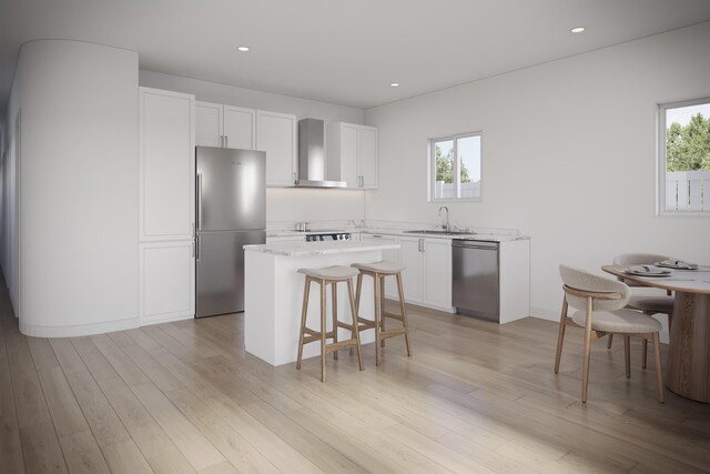 kitchen with wall chimney range hood, a center island, a sink, a breakfast bar area, and appliances with stainless steel finishes