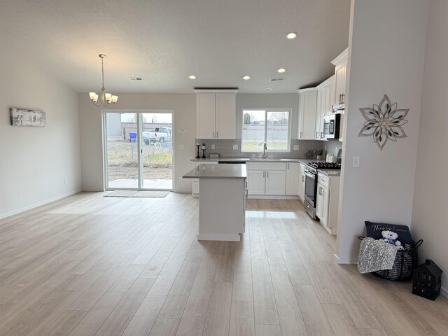 kitchen featuring stainless steel appliances, a sink, light wood-type flooring, a chandelier, and white cabinetry