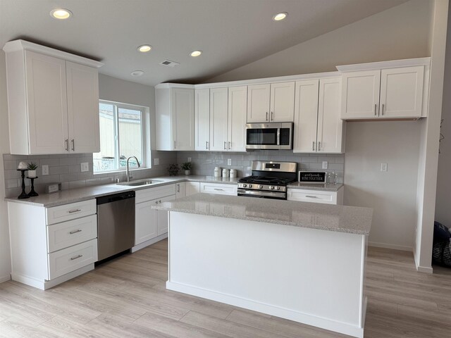 kitchen with white cabinets, stainless steel appliances, vaulted ceiling, a sink, and a center island