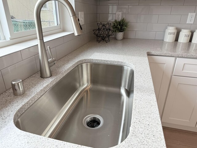 details with light stone counters, decorative backsplash, white cabinetry, and a sink