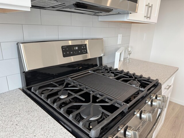 room details with light stone countertops, decorative backsplash, stainless steel range with gas stovetop, and white cabinetry