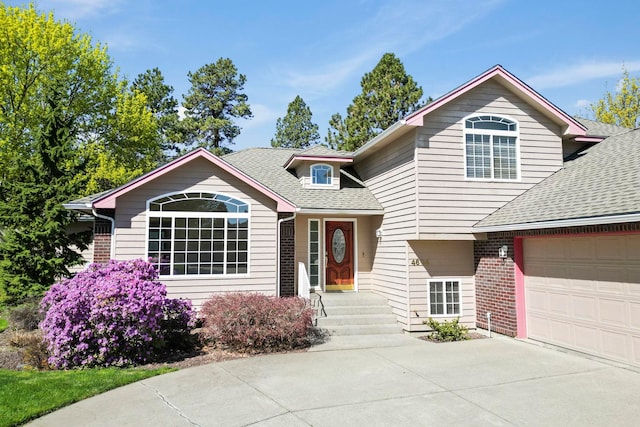 split level home with driveway, roof with shingles, brick siding, and a garage