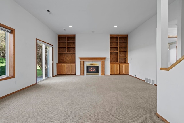 unfurnished living room with baseboards, a tile fireplace, built in shelves, and carpet
