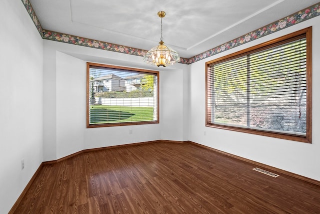 empty room featuring baseboards, a notable chandelier, wood finished floors, and visible vents