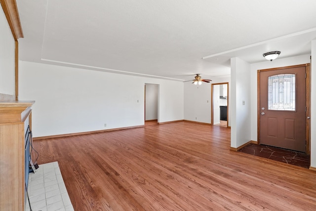 unfurnished living room featuring ceiling fan, baseboards, and light wood-style flooring