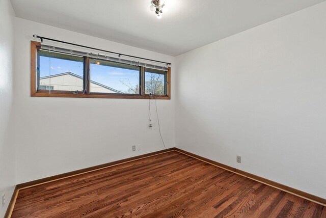 spare room with baseboards and dark wood-style flooring