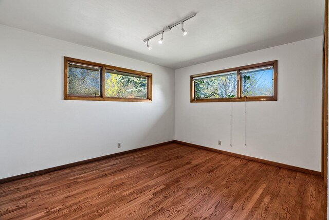 spare room with track lighting, wood finished floors, and baseboards
