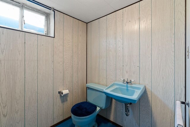 half bathroom with toilet, a sink, and wooden walls