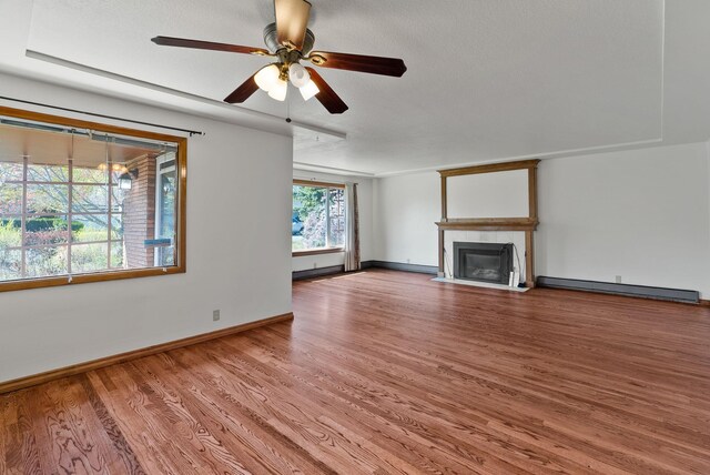 unfurnished living room featuring a baseboard heating unit, a fireplace with flush hearth, baseboards, a ceiling fan, and wood finished floors