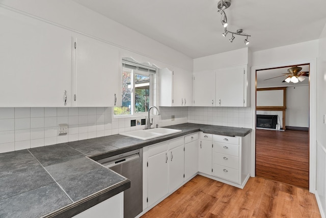 kitchen featuring dark countertops, light wood finished floors, stainless steel dishwasher, and a sink