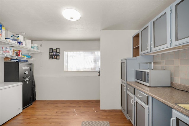 kitchen featuring light wood finished floors, white microwave, decorative backsplash, open shelves, and washer / dryer