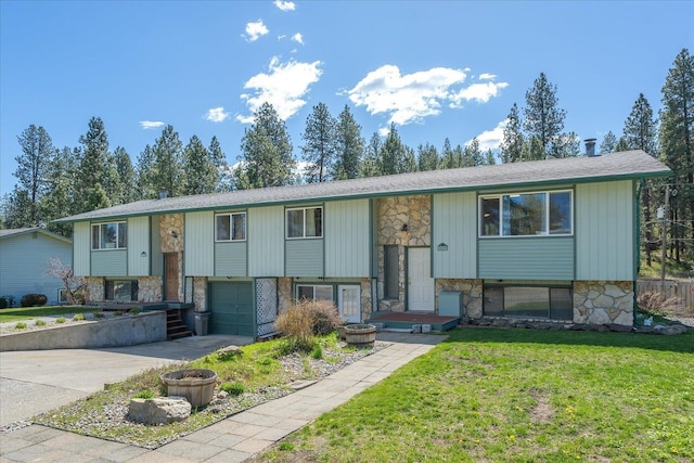 split foyer home featuring roof with shingles, stone siding, concrete driveway, an attached garage, and a front yard