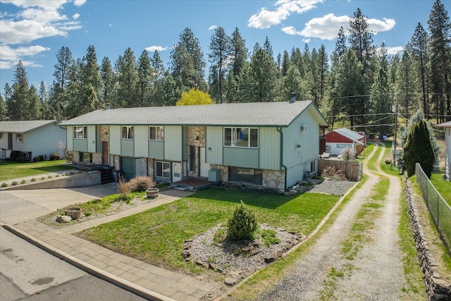 split foyer home featuring a front lawn, driveway, fence, and stone siding