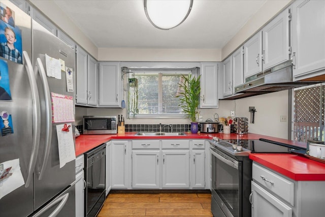 kitchen featuring white cabinets, under cabinet range hood, a sink, light wood-type flooring, and appliances with stainless steel finishes