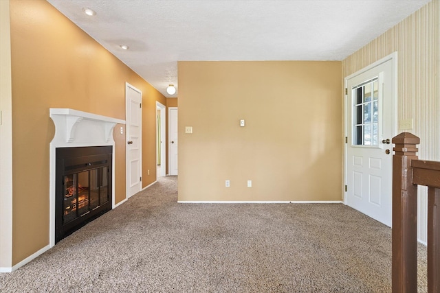 unfurnished living room featuring a glass covered fireplace, baseboards, and carpet flooring