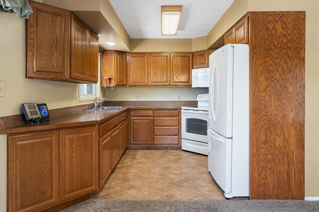 kitchen with brown cabinets, dark countertops, a sink, and white appliances