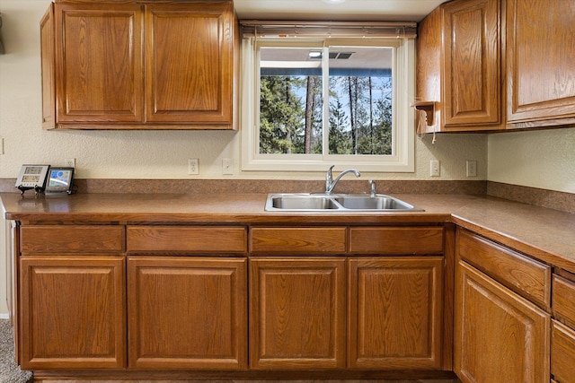 kitchen featuring dark countertops, a textured wall, visible vents, a sink, and brown cabinetry
