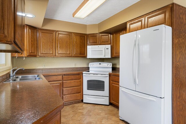 kitchen with brown cabinetry, white appliances, a sink, and dark countertops