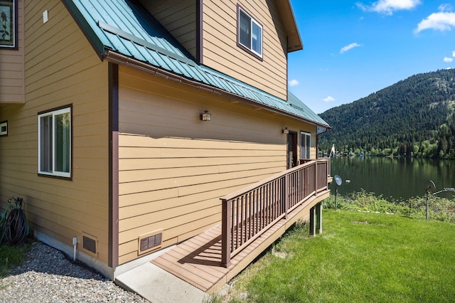 view of side of property featuring a lawn, a view of trees, a water and mountain view, and metal roof
