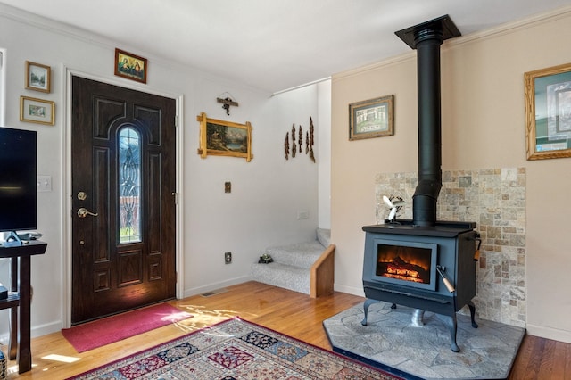 foyer featuring baseboards, wood finished floors, a wood stove, and crown molding