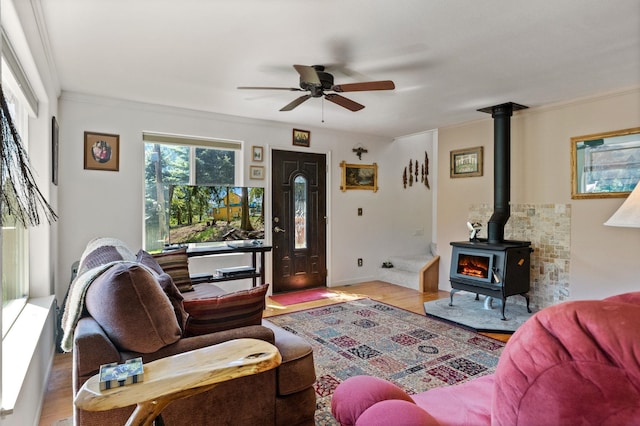 living area featuring wood finished floors, a wood stove, ornamental molding, and ceiling fan