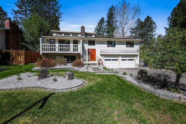 bi-level home with concrete driveway, an attached garage, fence, and a front lawn