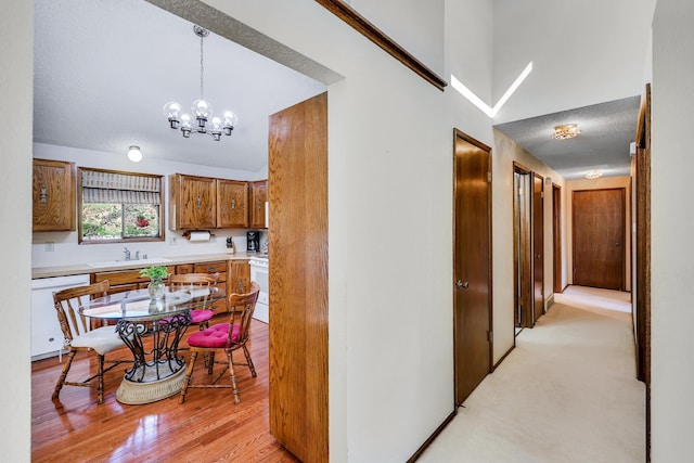 corridor with high vaulted ceiling, a sink, a chandelier, and light wood-style flooring