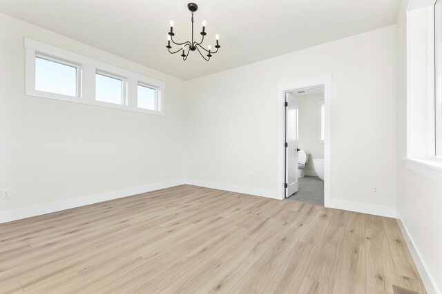 empty room featuring light wood-type flooring, baseboards, and a notable chandelier