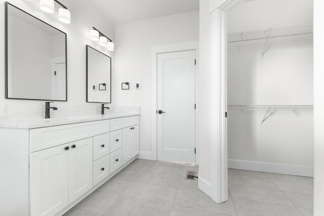 bathroom with a walk in closet, double vanity, baseboards, and a sink