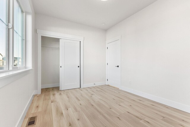 unfurnished bedroom featuring a closet, wood finished floors, visible vents, and baseboards