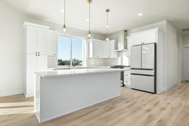 kitchen with wall chimney exhaust hood, freestanding refrigerator, white cabinetry, gas stove, and light countertops